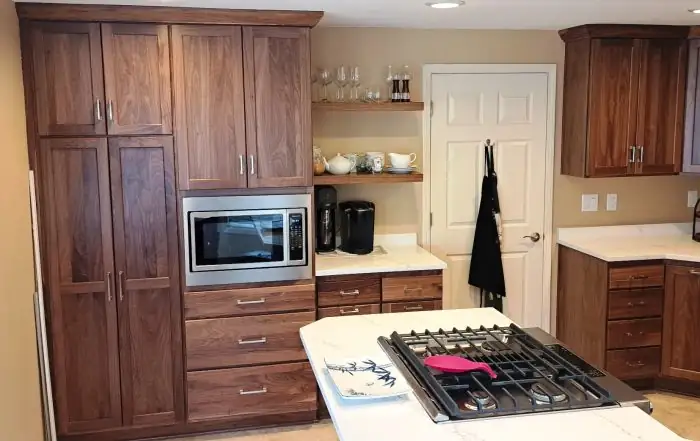 Kitchen with walnut cabinets, tall pantry wall with built-in microwave and a gas cooktop island