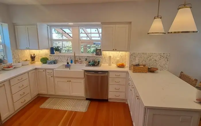 Kitchen with cream Shaker cabinets, white quartz counters, a mosaic tile backsplash and two cone pendants over a U-shaped layout