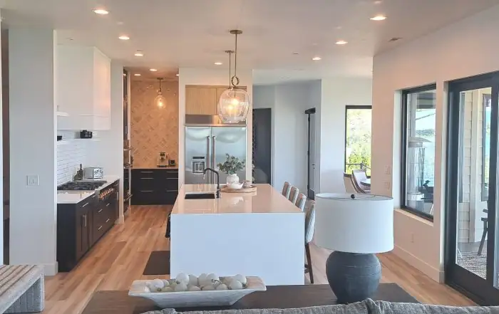 Bright open kitchen with white upper cabinets, dark base cabinets, a white waterfall island and glass pendants