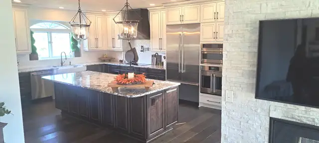 Kitchen with cream painted cabinets, a dark stained island with a granite top, lantern pendants and a stacked stone accent wall
