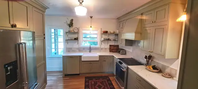 Kitchen with sage painted cabinets, farmhouse sink, open shelves and a painted range hood