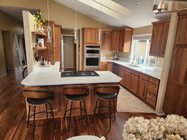 Kitchen with cherry cabinets, large white quartz island with gas cooktop and leather bar stools